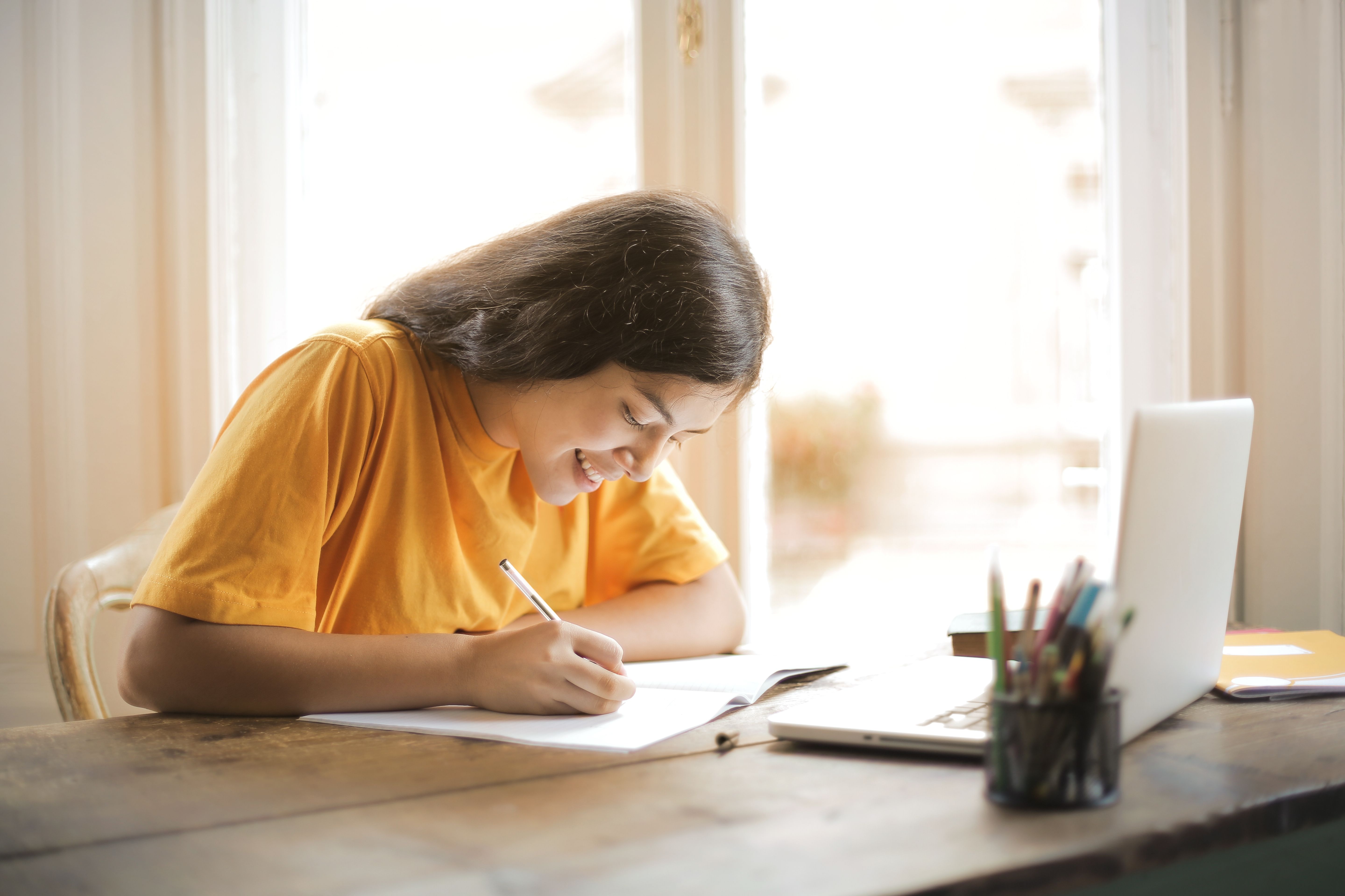 Young woman studying with a laptop and notepad at home, focused on her assignment